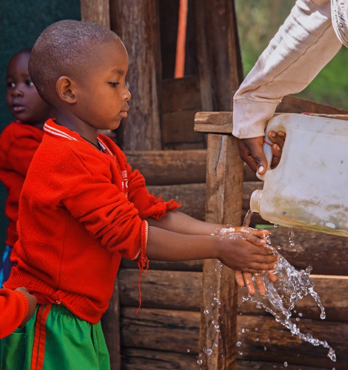 boy-washing-hands-19024870 Young child washing hands in a rural area of Uganda, promoting hygiene awareness.